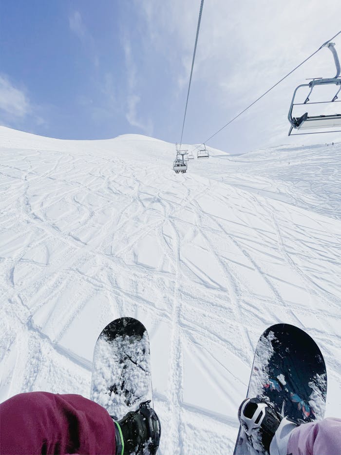 Home View from a ski lift over snowy slopes with snowboarders, showcasing winter sports adventure.